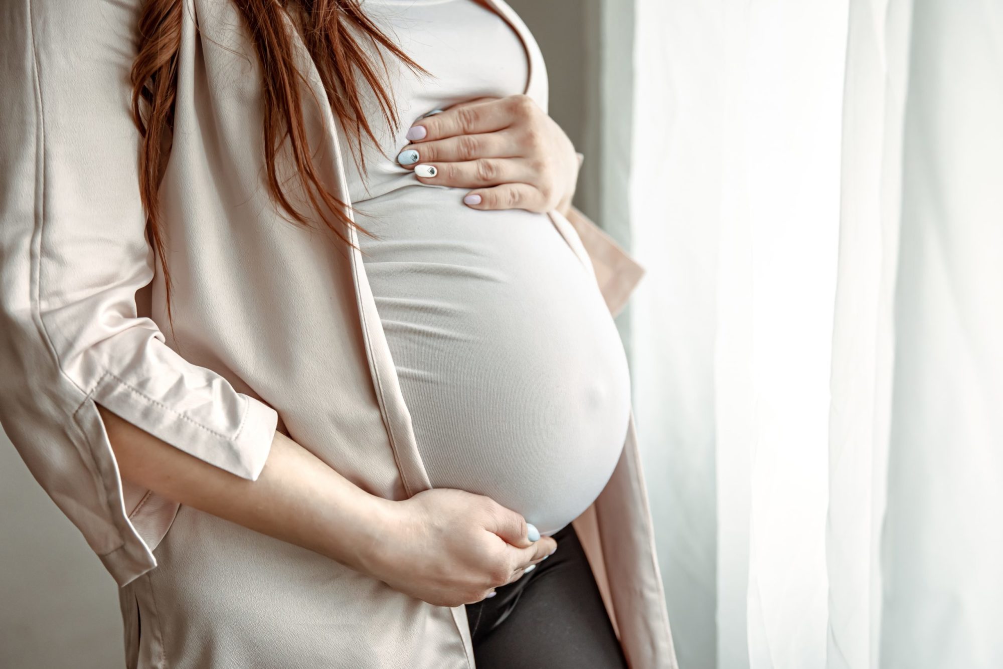 Close up of belly of a pregnant woman standing by the window.