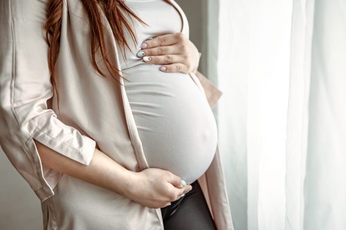 Close up of belly of a pregnant woman standing by the window.