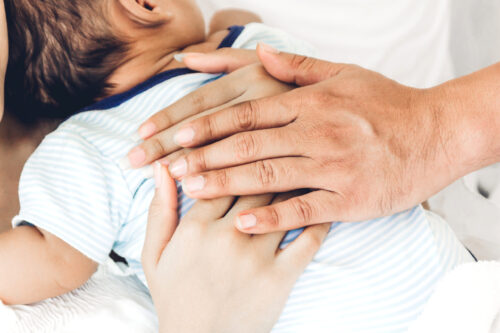 Mother and father holding baby in her arms in a white bedroom.Lo